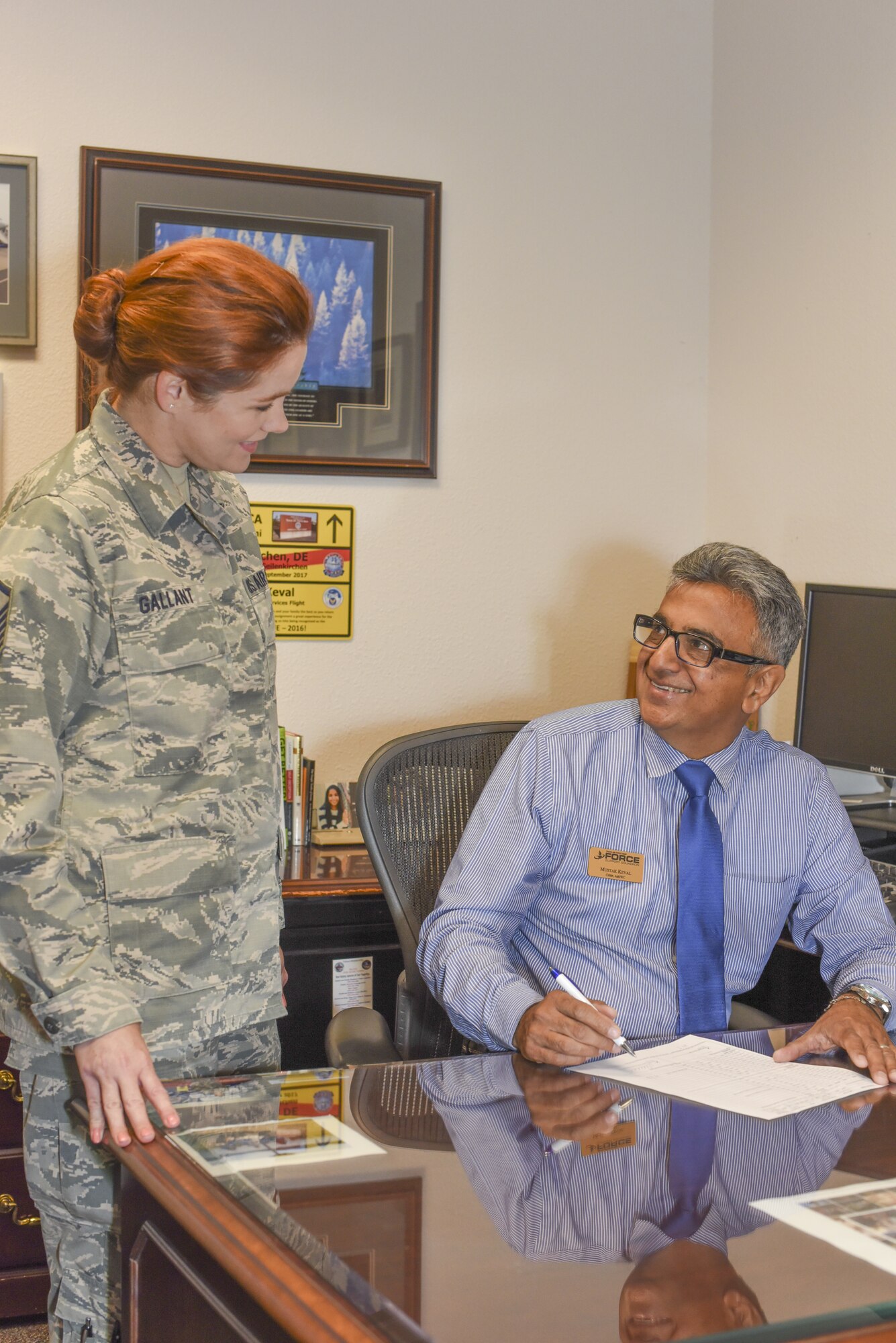Mustak Keval, 60th Force Support Squadron Airman and Family Readiness Center flight chief, assists Master Sgt. Erine Gallant, 60th FSS AFRC NCO in-charge, July 23, 2018, at Travis Air Force Base, Calif. Keval, a Ugandan refugee spent more than 20 years in the U.S. Air Force and continues to serve Airmen and their families at the AFRC. (U.S. Air Force photo by Staff Sgt. Amber Carter)