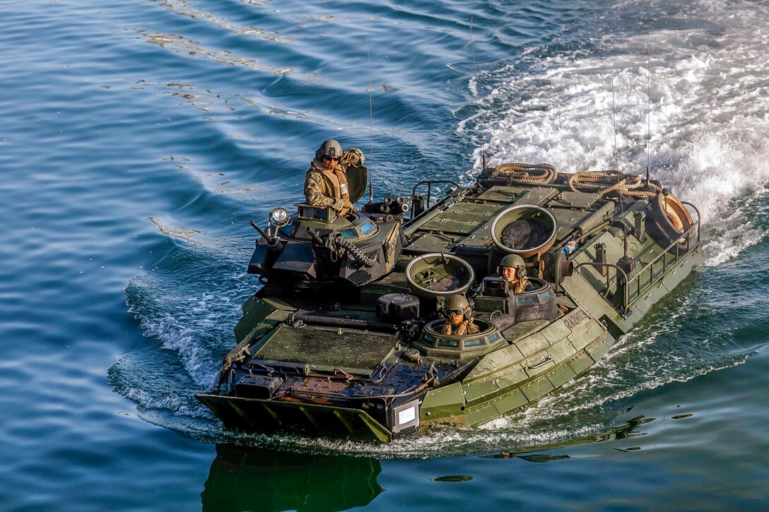Marines aboard an assault amphibious vehicle travel through blue waters.