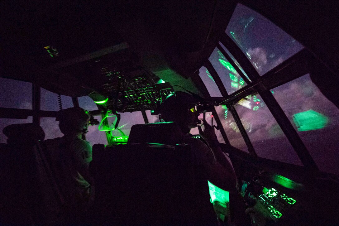 Airmen look out from a dark cockpit at purple sky.
