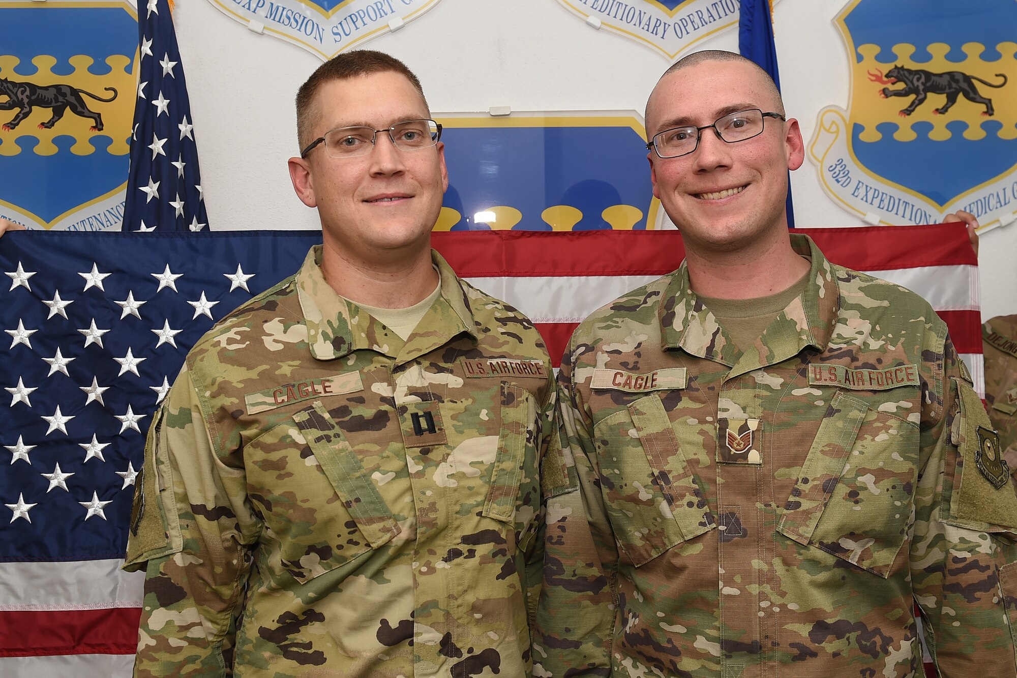 Two Airmen pose for a photo in front of an American flag