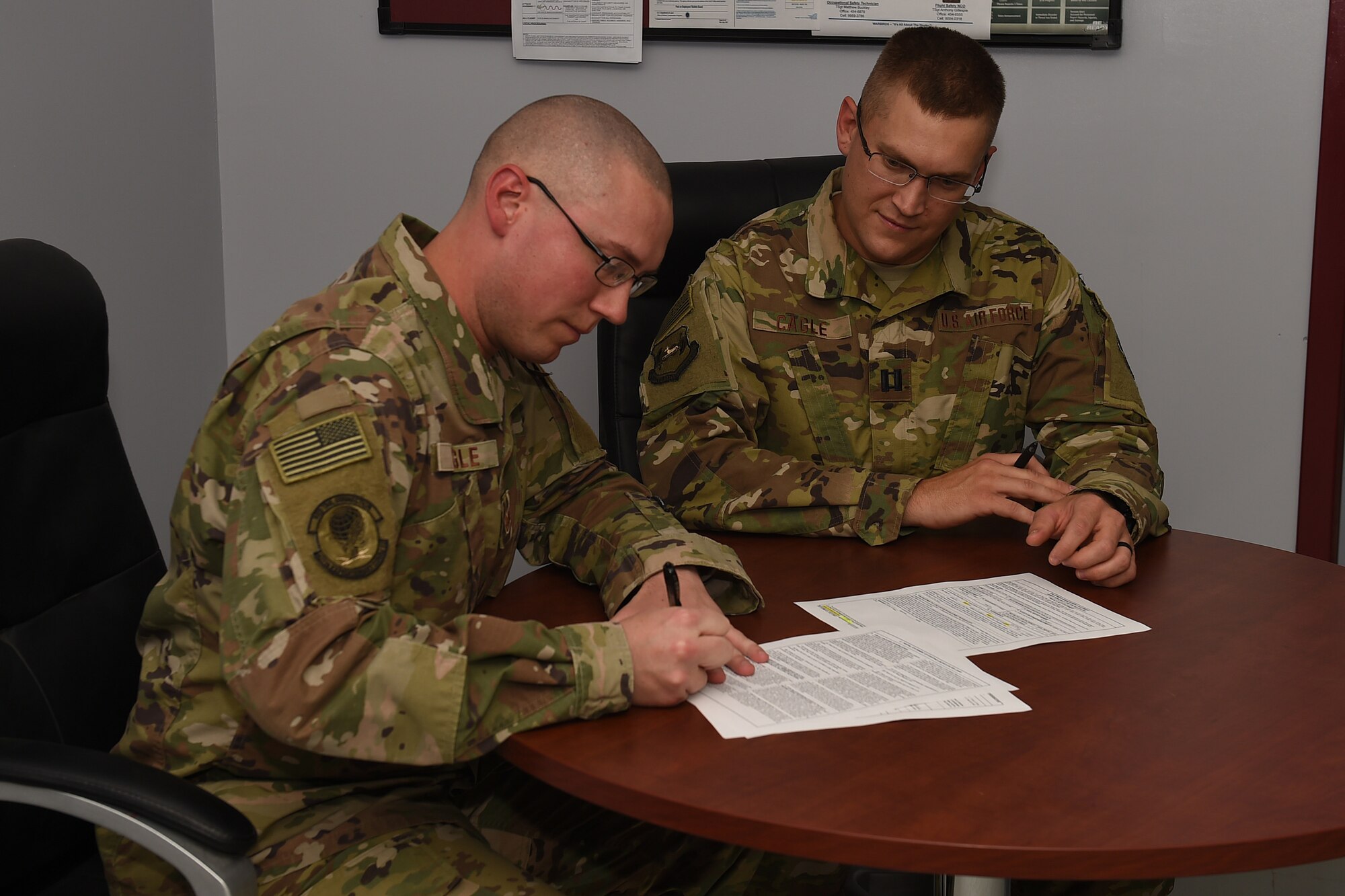 Two Airmen sit at a desk a sign paperwork