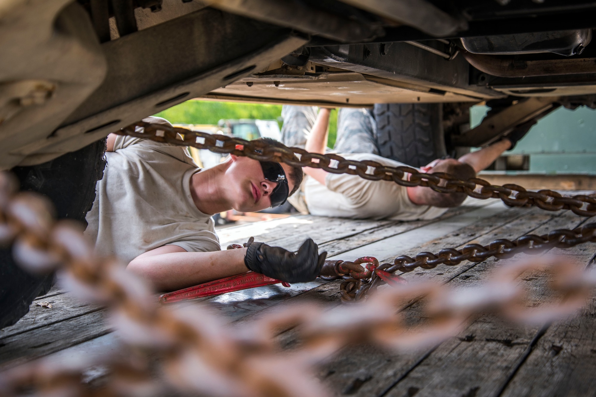 U.S. Air Force Airman 1st Class Dennis Fite, left, and Airman 1st Class Brinkley Owens, both 100th Logistics Readiness Squadron ground transportation operators, secure vehicle to a trailer at RAF Mildenhall, England July 20, 2018. Chains keep the vehicle more secure on the trailer, rather than using regular tie down straps. (U.S. Air Force photo by Senior Airman Christine Groening)