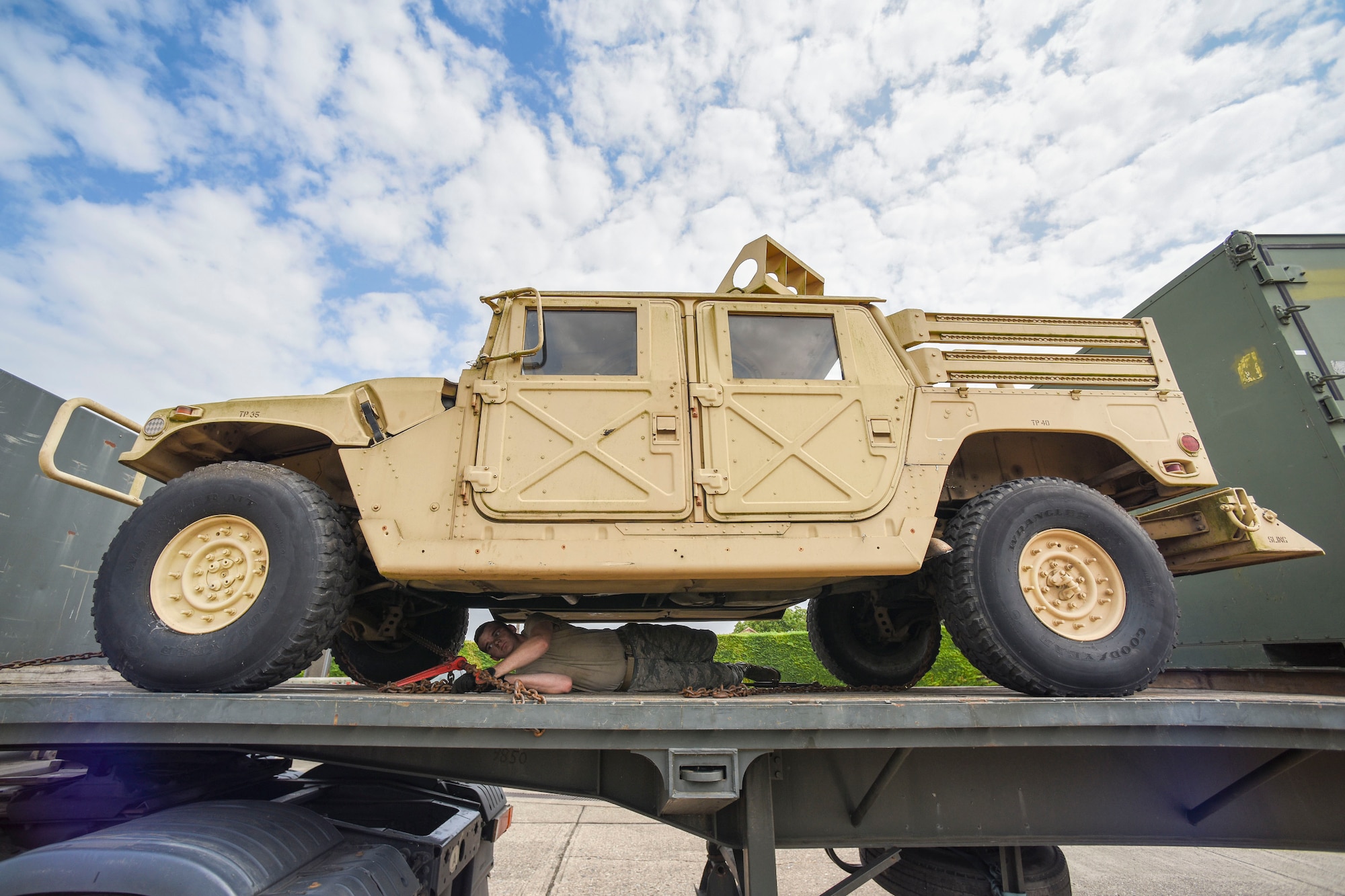 U.S. Air Force Airman 1st Class Brinkley Owens, 100th Logistics Readiness Squadron ground transportation operator, conducts tie down procedures on a HUMVEE on RAF Mildenhall, England, July 20, 2018. Chains keep the vehicle more secure on the trailer, rather than using regular tie down straps. (U.S. Air Force photo by Senior Airman Christine Groening)