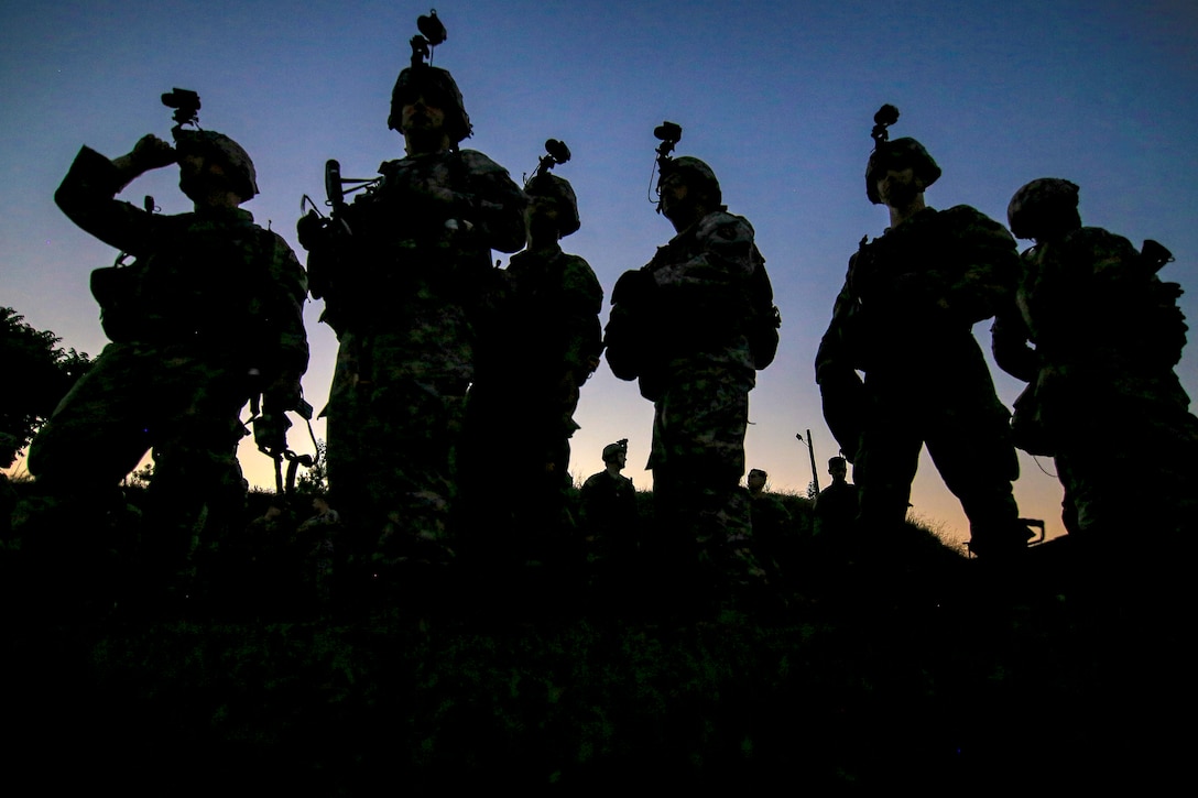 Soldiers stand near each other and are silhouetted by the setting sun.