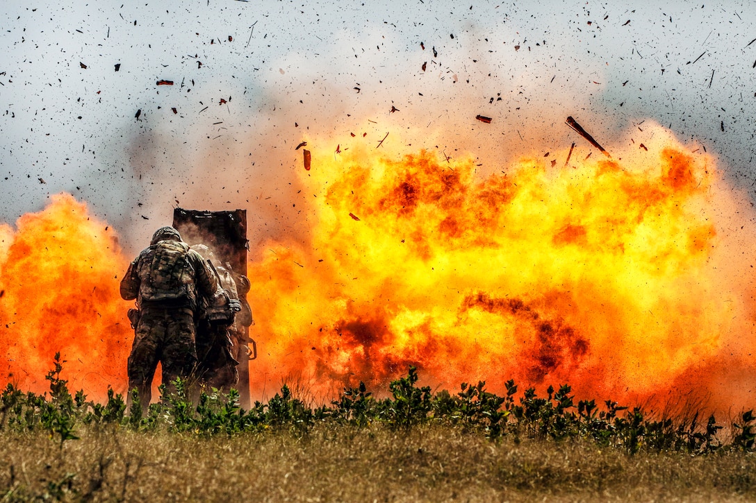 Soldiers brace themselves behind a shield as a detonation creates a huge fireball, sending pieces of concrete in the air.