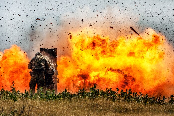 Soldiers brace themselves behind a shield as a detonation creates a huge fireball, sending pieces of concrete in the air.