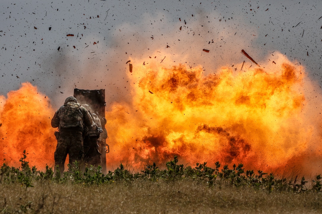 Soldiers create a fiery explosion to breach a concrete wall.
