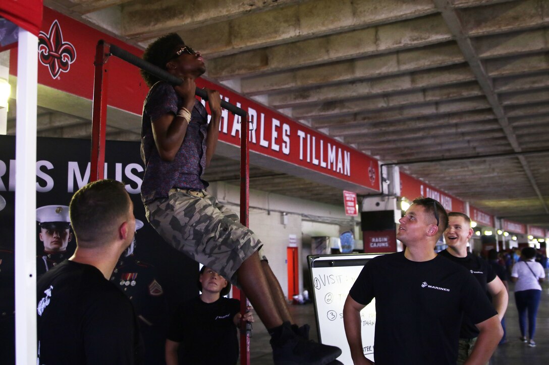Marines with the Marine Forces Reserve Band encourage a Drum Corps International event attendee on the pull-up bar at the Cajundome Convention Center in Lafayette, Louisiana, July 23, 2018. The Drum Corps International creates a stage for the Marine Corps to engage in education, competition and the promotion of individual growth. (U.S. Marine Corps photo by Sgt. Nathaniel C. Cray)