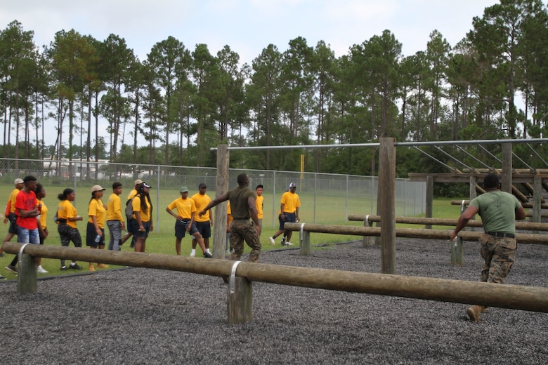 U. S. Marine Corps instructors perform a demonstration of proper techniques on maneuvering the obstacle course with dozens of Navy and Marine Corps Junior Reserve Officers Training Corps cadets. More than 40 cadets spent an intense five days at Marine Corps Logistics Base Albany for its first-ever summer camp. Each cadet experienced a week-long taste of basic leadership training. (U.S. Marine Corps photo by Re-Essa Buckels)