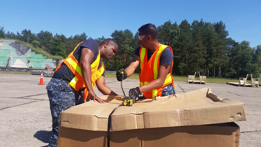 Defense Logistics Agency Reservists, Navy Logistics Specialist Petty Officer 2nd Class Jay Washington and Navy Logistics Specialist Petty Officer 2nd Class Daniel Henderson use a strapping tool in Powidz Air Base, Poland June 6 during Saber Strike 18. Saber Strike is an annual exercise conducted at various locations throughout Poland, Estonia, Latvia and Lithuania with about 18,000 attendees from 19 different countries.  (Photo by Navy Lt. Cmdr. Allison Adams Jones, Executive Officer, DLA Expeditionary Distribution Support Unit Norfolk.)