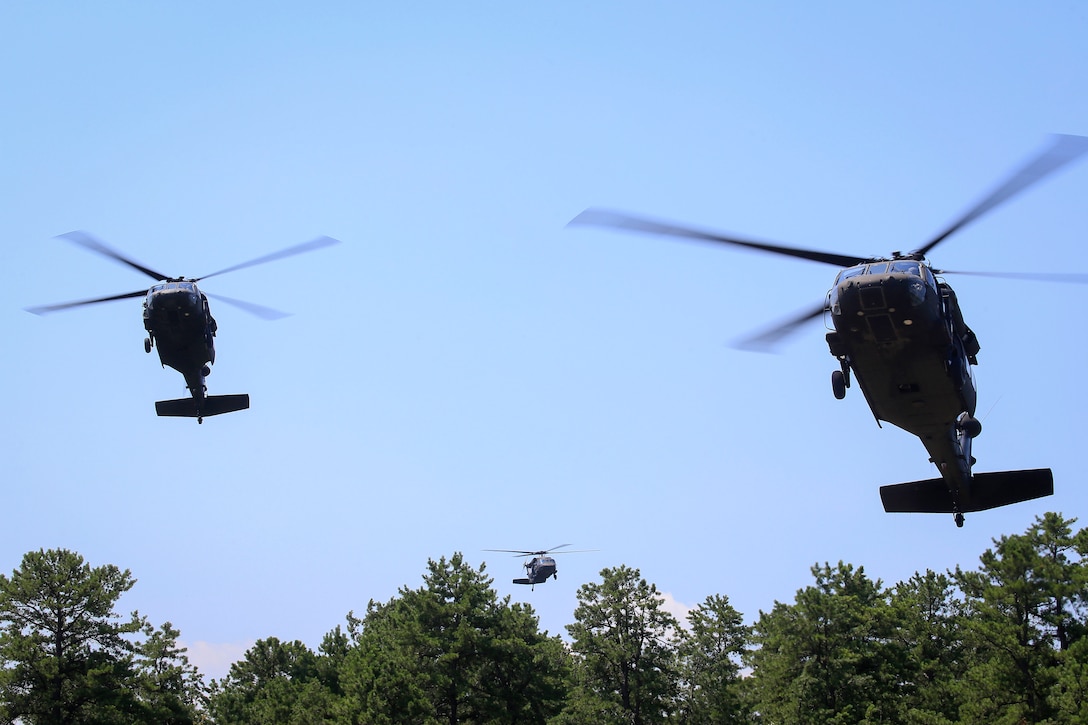 Three Army UH-60L Black Hawk helicopters hovering, prepare to land and pickup soldiers.