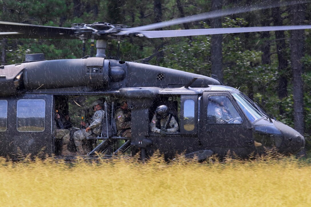 An Army crew chief checks for clearance out the side of a helicopter.