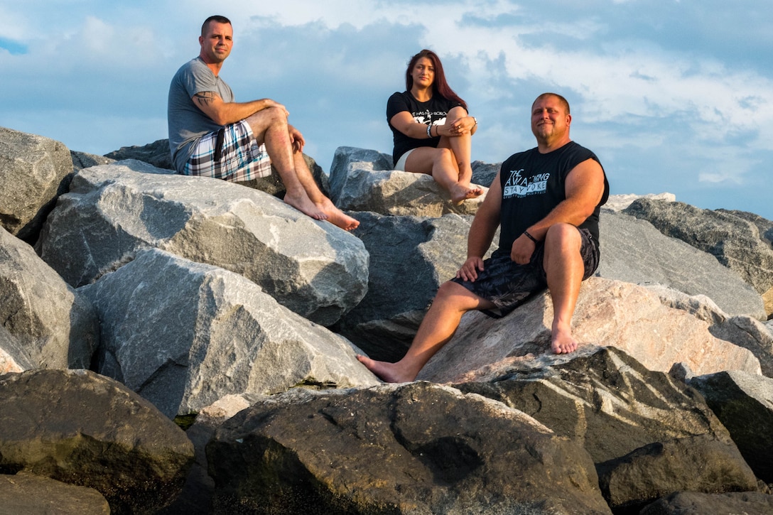 Three people sit on large rocks on a beach.