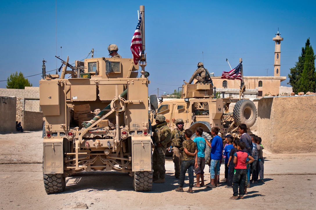 A group of children gather around a U.S. military convoy conducting a patrol.