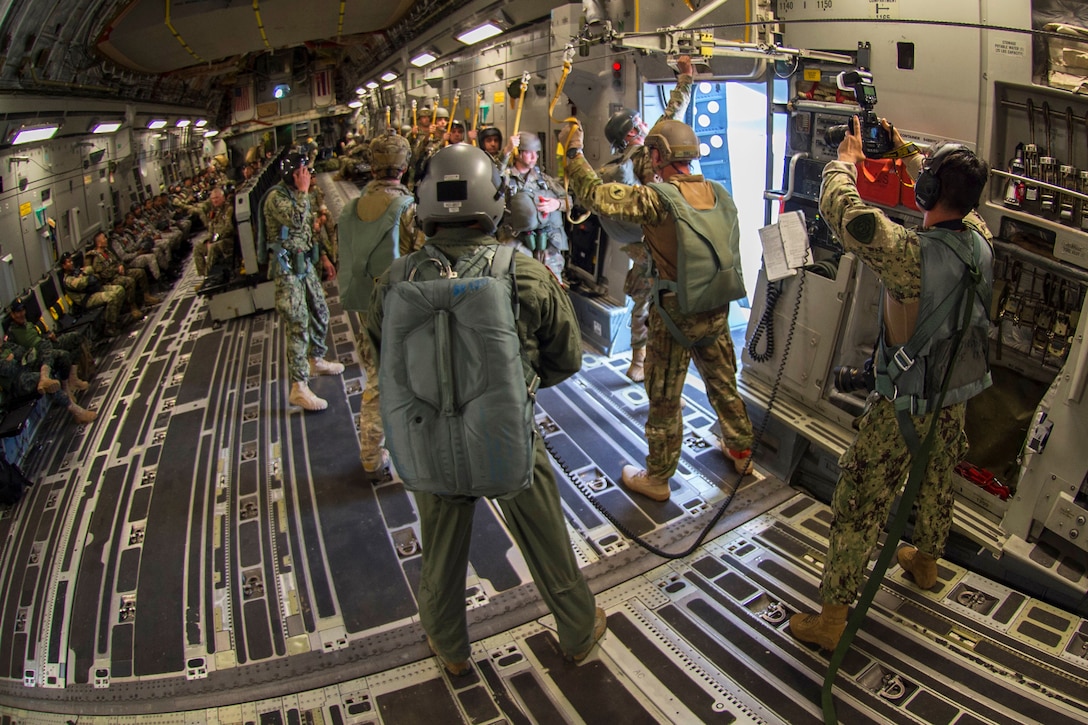 A Navy sailor records static line parachute jumpers as they prepare to exit a C-17 Globemaster III during airborne training operations.