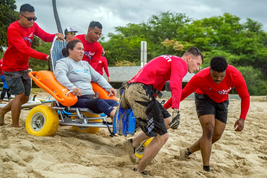 Marines pull a person in a rolling chair down a beach.