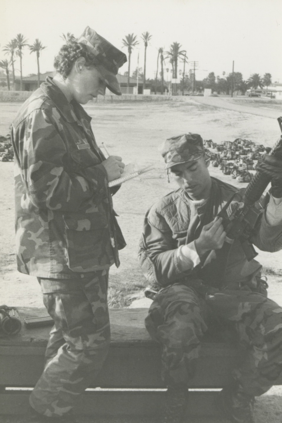 Cpl. Barbara Cogburn, primary marksmanship instructor (PMI) with Weapons and Field Training Battalion, Marine Corps Recruit Depot San Diego, assists a Marine during a rifle qualification at Edson Range on Marine Corps Base Camp Pendleton, 1985. Cogburn, a food service specialist, became the first school-trained female PMI in 1984. PMIs act as an instructor to other Marines on how to precisely handle and fire weapon systems on small arms ranges.