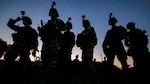 Soldiers stand near each other and are silhouetted by the setting sun.