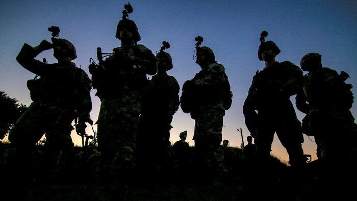 Soldiers stand near each other and are silhouetted by the setting sun.