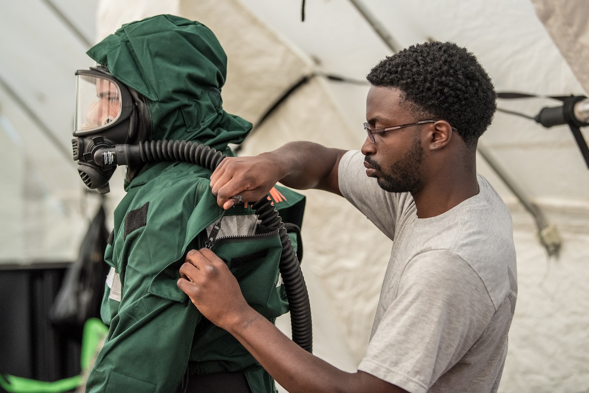 Airman First Class Anthony Cirwithian (right), a member of the Kentucky Air National Guard's Fatality Search and Recovery Team, zips up a MT94 chemical, biological, radiological and nuclear defense suit for Senior Airman Ben Bohannon, another FSRT member, at Rough River State Resort Park in Falls of Rough, Ky., on July 18, 2018. Thirteen members of the 123rd Airlift Wing participated in the three-day exercise to simulate the recovery and repatriation of fallen service members. (U.S. Air National Guard photo by Master Sgt. Phil Speck)