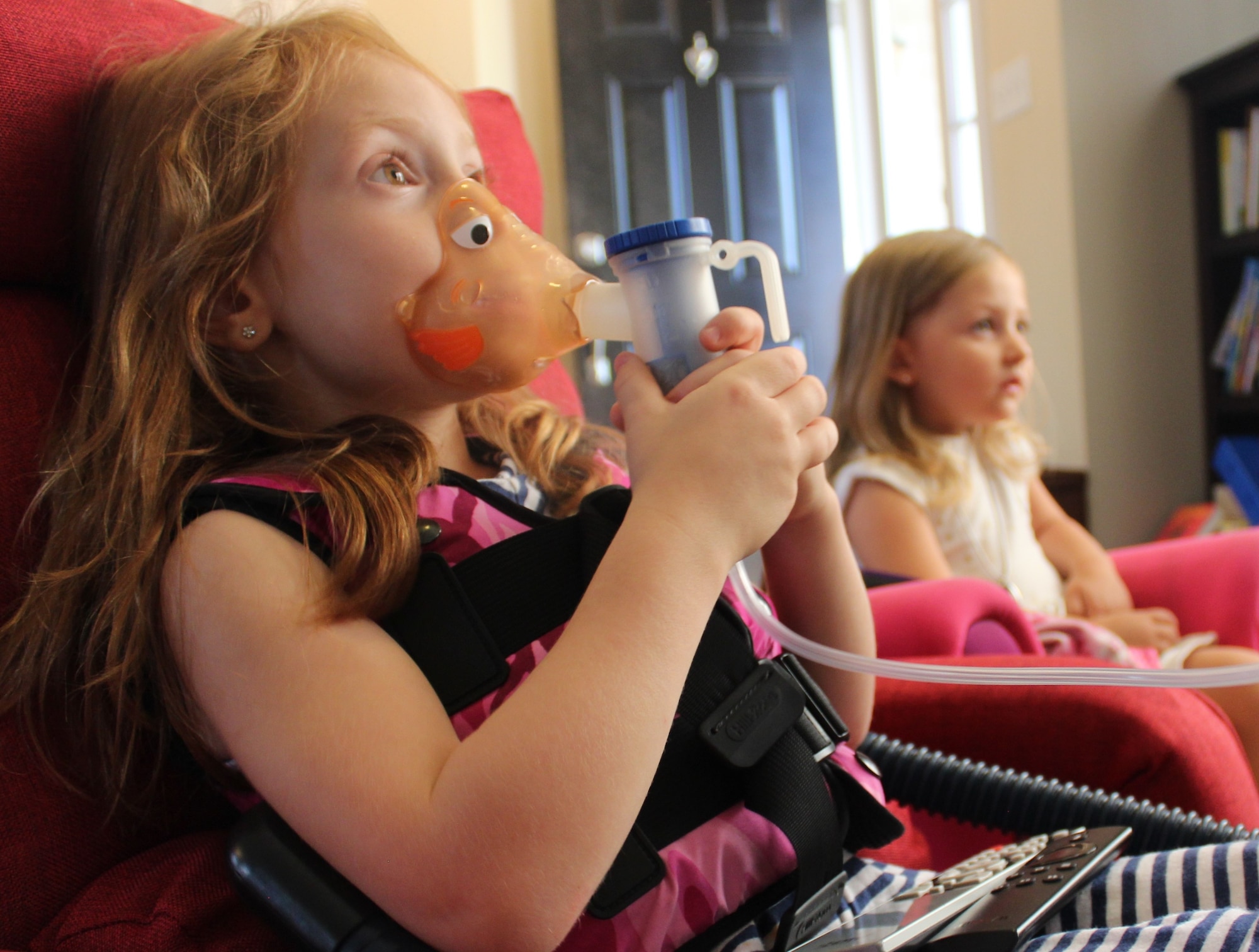 Five-year old Aubrey Inman watches television during a treatment for cystic fibrosis while her sister, three-year old Adalyn, keeps her company. At least twice a day, Aubrey is required to take several medications, use a nebulizer and wear a vest that that fills with air and pulses around the body to shake up the lungs to help break up the mucus. (U.S. Air Force Photo/Stacey Geiger)