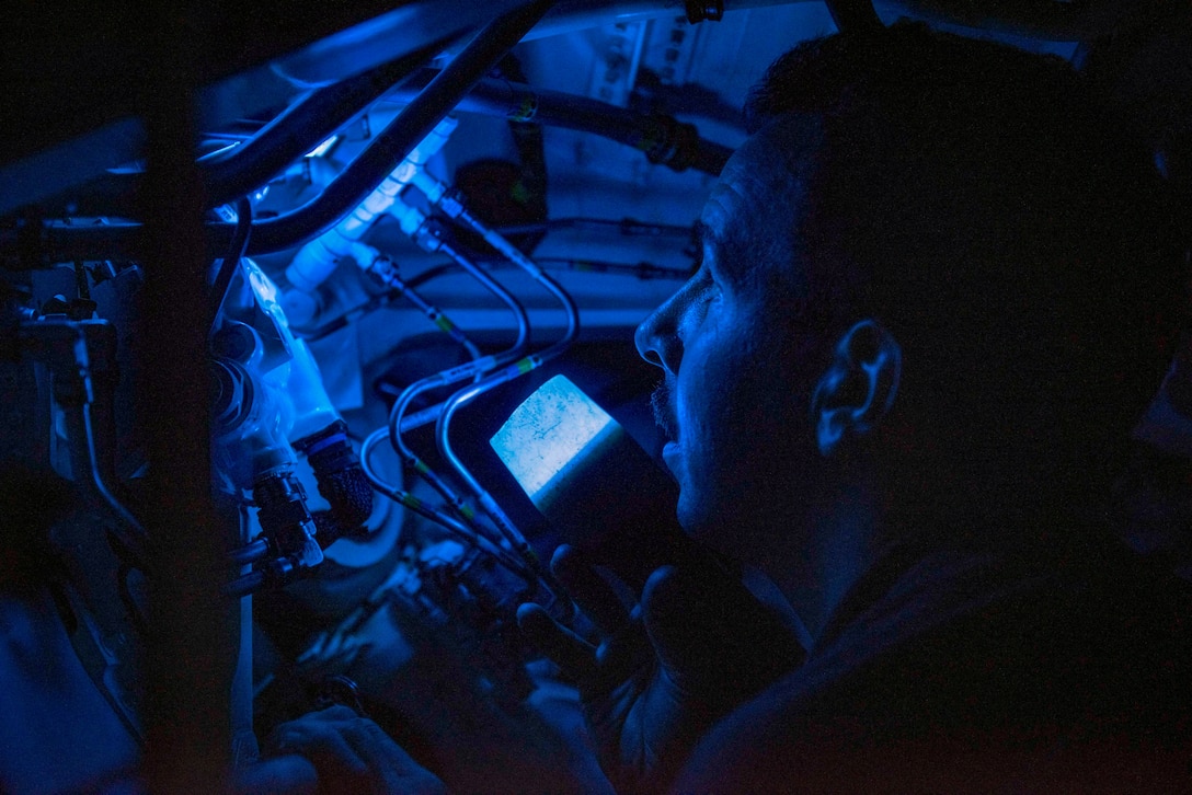 A sailor looks at equipment illuminated with blue light.