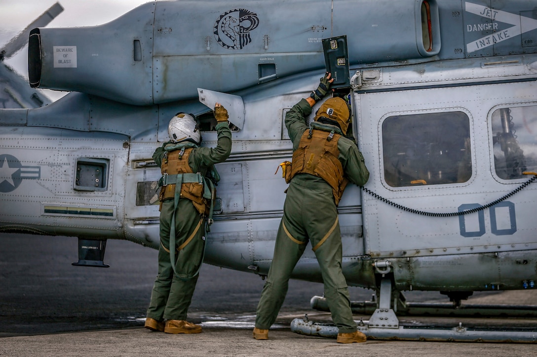 Two Marines, shown from behind, inspect the fuselage of an aircraft.