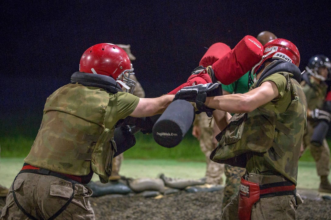 A Marine in a red helmet hits another Marine in a red helmet with a red stick.