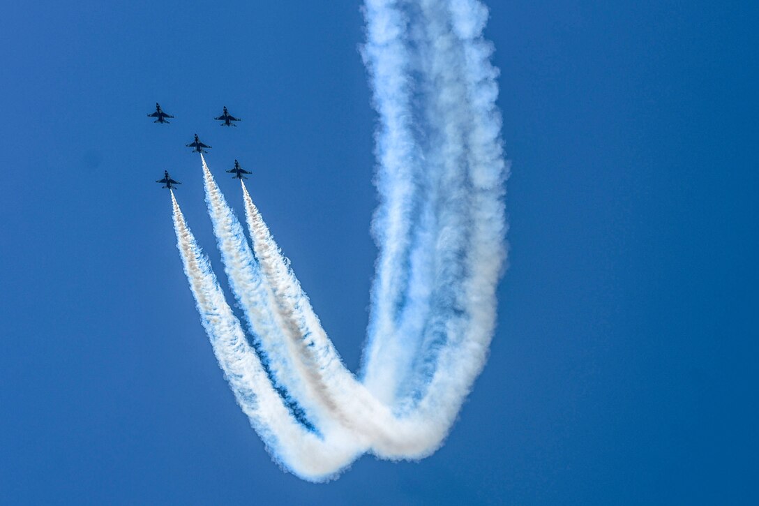 Five aircraft fly in formation, leaving U-shaped smoke trails in their wake.
