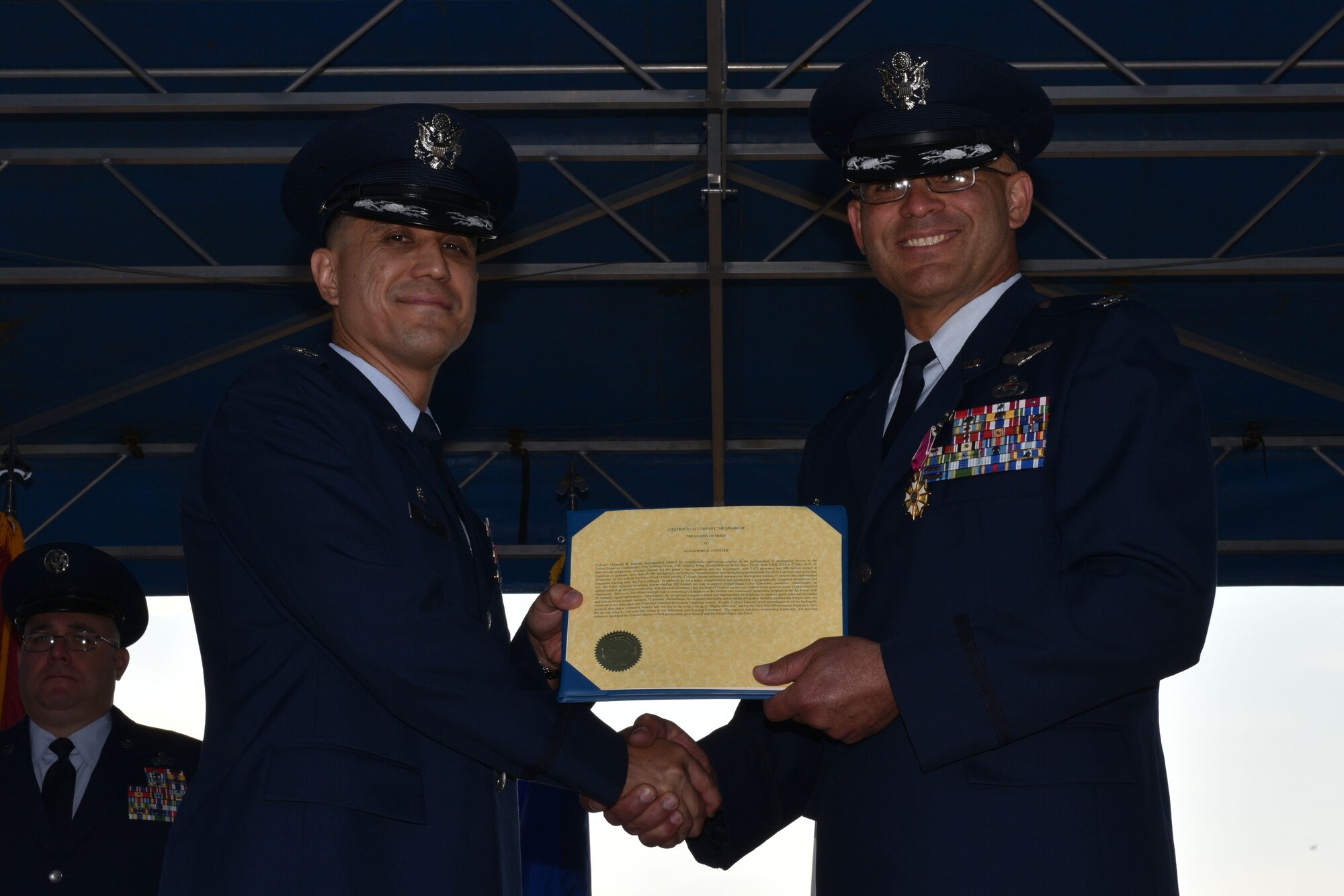 U.S. Air Force Col. Ricky Mills, 17th Training Wing commander, presents Col. Alex Ganster, 17th Training Group outgoing commander, with a Legion of Merit certificate during the 17th TRG Change of Command on the parade field on Goodfellow Air Force Base, Texas, July 27, 2018. For two years, Ganster led the group’s four squadrons and one detachment, with 2,472 personnel and $400 million in resources, to graduate more than 28,500 students from all five branches and more than 25 nations. (U.S. Air Force photo by Senior Airman Randall Moose/Released)