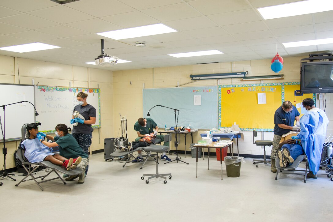 Dentists and dental technicians from the U.S. Air Force, Air Force Reserve and Navy Reserve provide dental treatments for local residents in Millen, Ga., July 15, 2018, during the East Central Georgia Innovative Readiness Training. From left to right, U.S. Air Force Tech. Sgt. Kay Ankerich, of Hartwell, Ga., a dental technician with the Air Force Reserve’s 94th Aeromedical Staging Squadron, Dobbins Air Reserve Base, Ga., takes x-rays of young girl with Navy Reserve Hospital Corpsman Petty Officer Second Class Kiara Schuster, of Stevens Point, Wisc., a general medic with the Expeditionary Medical Facility Great Lakes, Capt. Ben Winston, dentist for the 72nd Dental Squadron, Tinker Air Force Base, Okla., provides treatment for a young boy and Col. Clifford Zdanowicz, of Balitmore, Md., a dentist and Tech. Sgt. Jacqueline Maragh, of Felton, Del., a dental technician for the 512th Aerospace Medical Squadron, Dover Air Force Base conduct an extraction for a local resident. An IRT provides hands-on, real-world training to improve readiness and interoperability for service members in complex contingency environments while providing key services for American communities. (U.S. Air Force photo by Master Sgt. Theanne Herrmann)