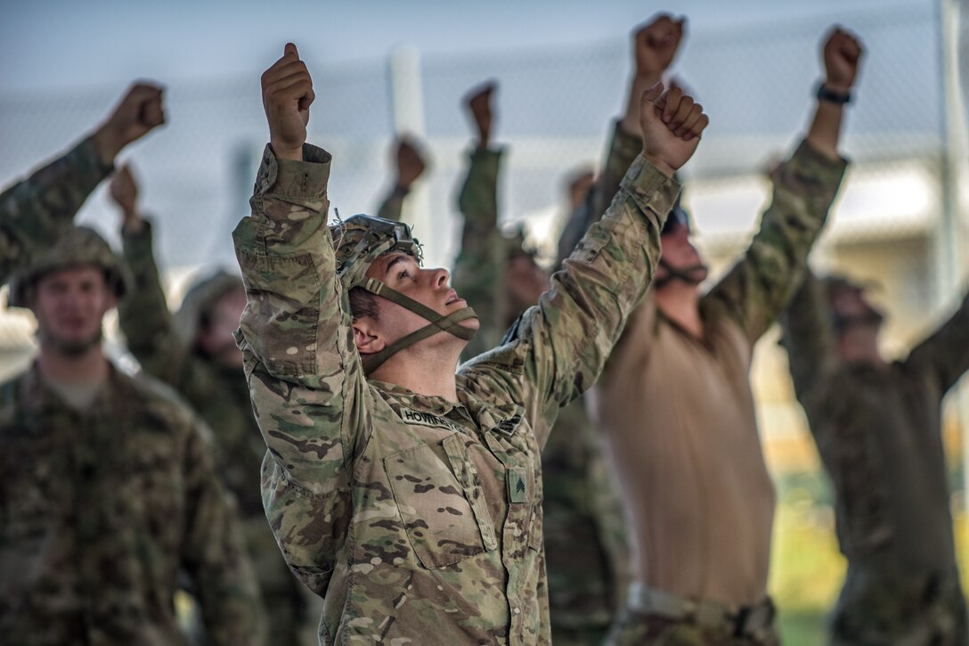 Paratroopers extend their arms in the air while looking up.