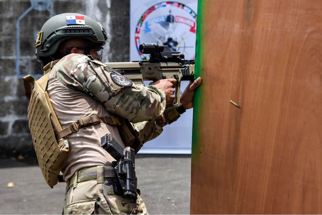 A Panamanian commando fires his weapon at targets from behind a wooden partition.