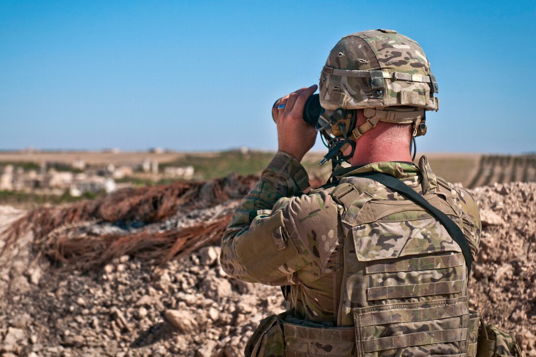 A U.S. soldier looks through binoculars to make visual contact with Turkish soldiers.