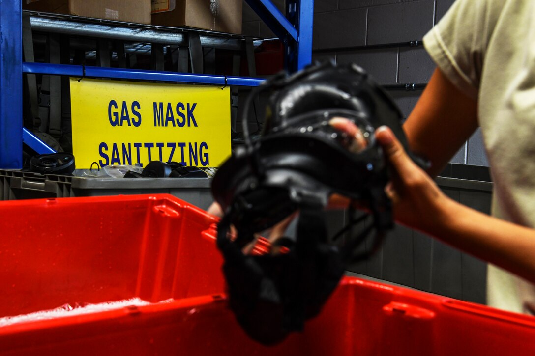 An airman rinses a gas mask in a sanitizing solution.