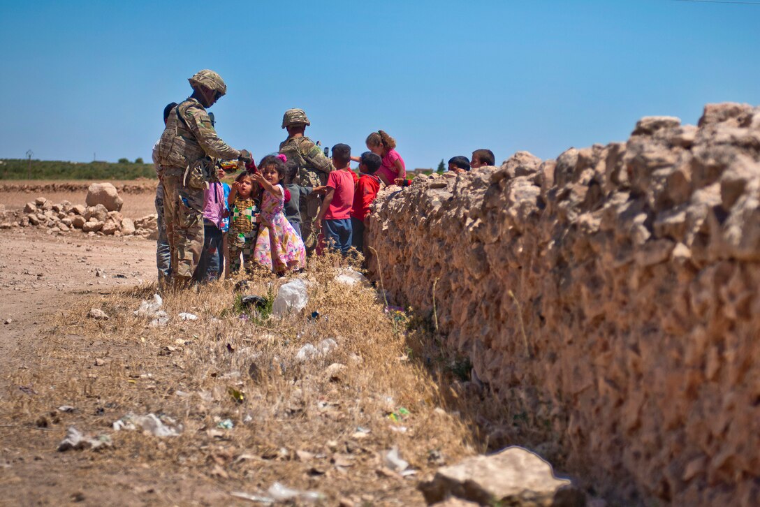 U.S. soldiers interact with and hand out candy to a group of children.