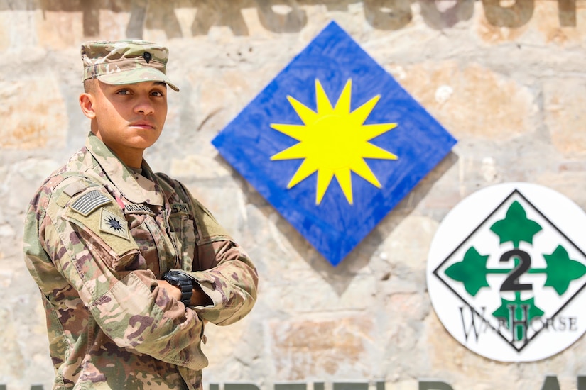 A soldier stands in front of the 40th Infantry Division logo.