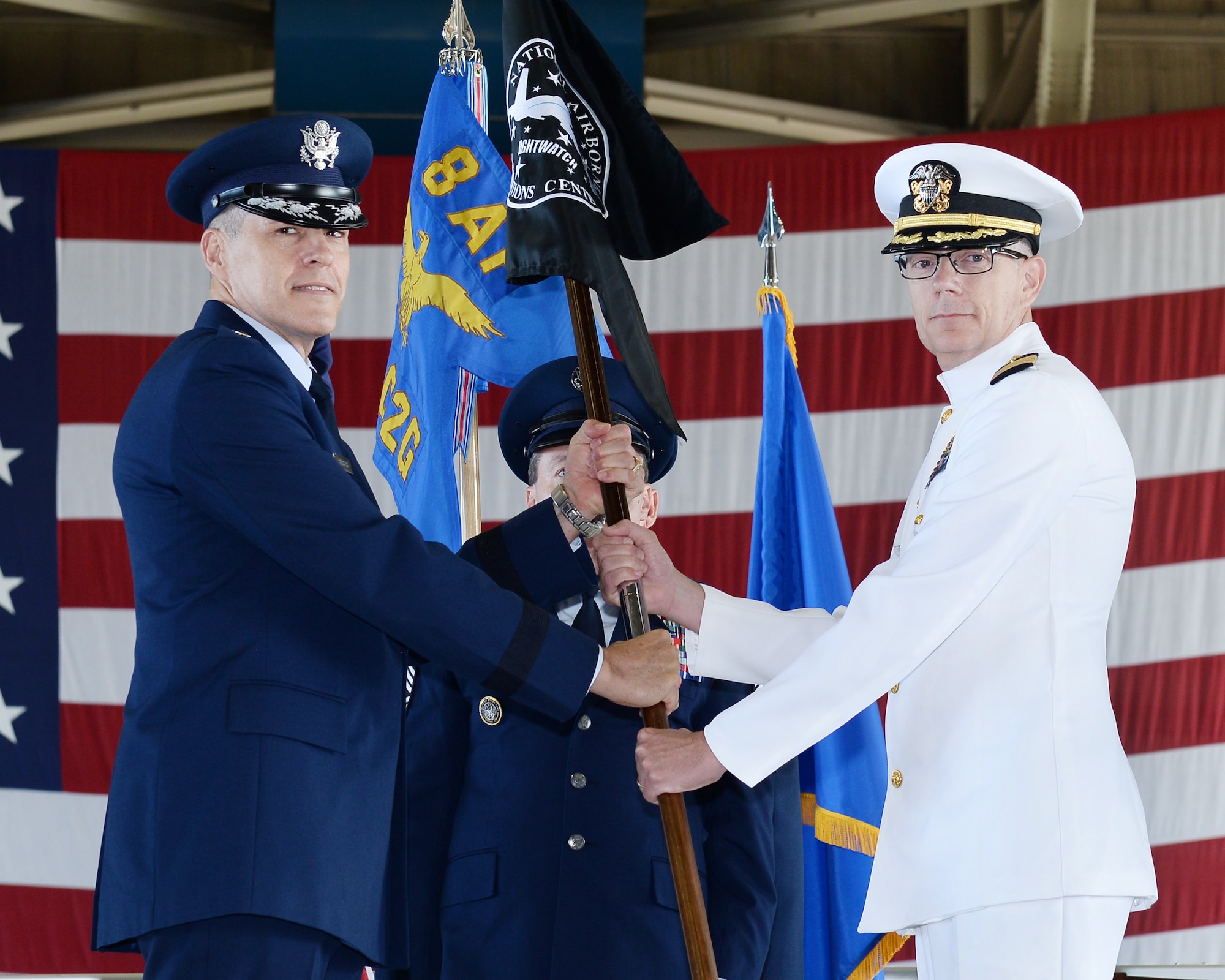 U.S. Air Force Maj. Gen. Thomas Bussiere, Eighth Air Force and Joint-Global Strike Operations Center commander (left), accepts the National Airborne Operations Center's guidon from U.S. Navy Capt. Dennis Crews, outgoing NAOC commander (right), during the dual-595th Command and Control Group and National Airborne Operations Center change of command ceremony July 27, 2018, at Offutt Air Force Base, Nebraska as a single commander assumed responsibility for both organizations. Passing of the guidon is a time-honored military tradition signifying the transfer of command.(U.S. Air Force photo by Charles Haymond)