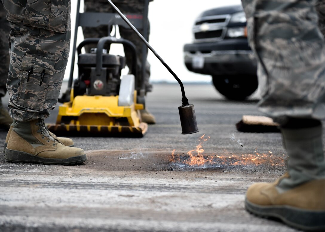 Airmen from Spangdahlem Air Base’s 52nd Civil Engineer Squadron use a torch to make asphalt malleable while Staff Sgt. David Springsteen, a pavements and construction helper from the 910th Civil Engineer Squadron, prepares a compactor on the Spangdahlem flightline, July 12, 2018.