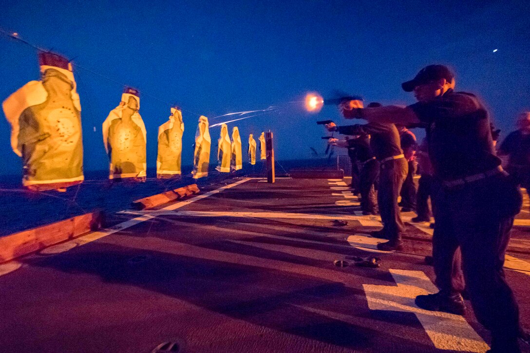 Sailors fire pistols on the deck of a ship at sea at night.