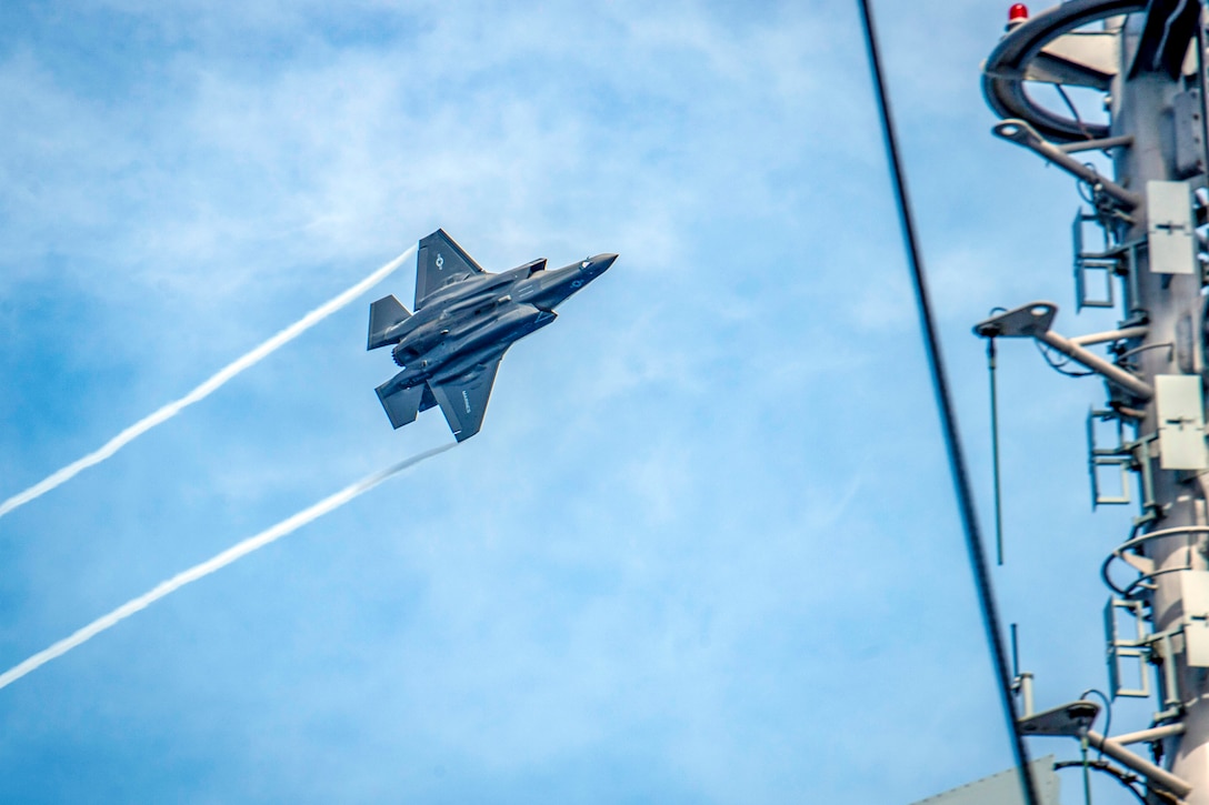 An airplane flies sideways close the a naval ship.