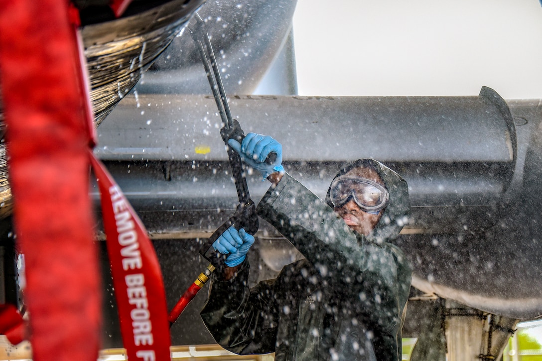 An airman washes a plane using a pressure washer.