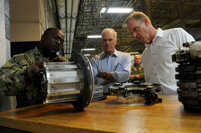 Navy Petty Officer 2nd Class Karil Courtenay, an aviation structural mechanic assigned to Fleet Readiness Center Mid-Atlantic Oceana in Virginia Beach, Va., discusses a hydraulic system part with Deputy Defense Secretary Patrick M. Shanahan, right, and Navy Secretary Richard V. Spencer, during their visit to the center, July 25, 2018. DoD photo by Lisa Ferdinando