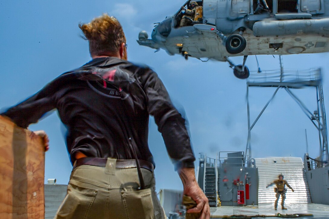 Winds from a hovering helicopter whips the shirts of two marines