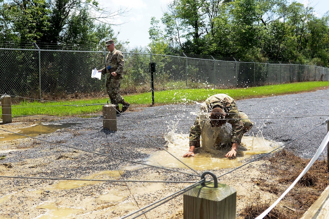 A soldier low crawls under the wire obstacle.