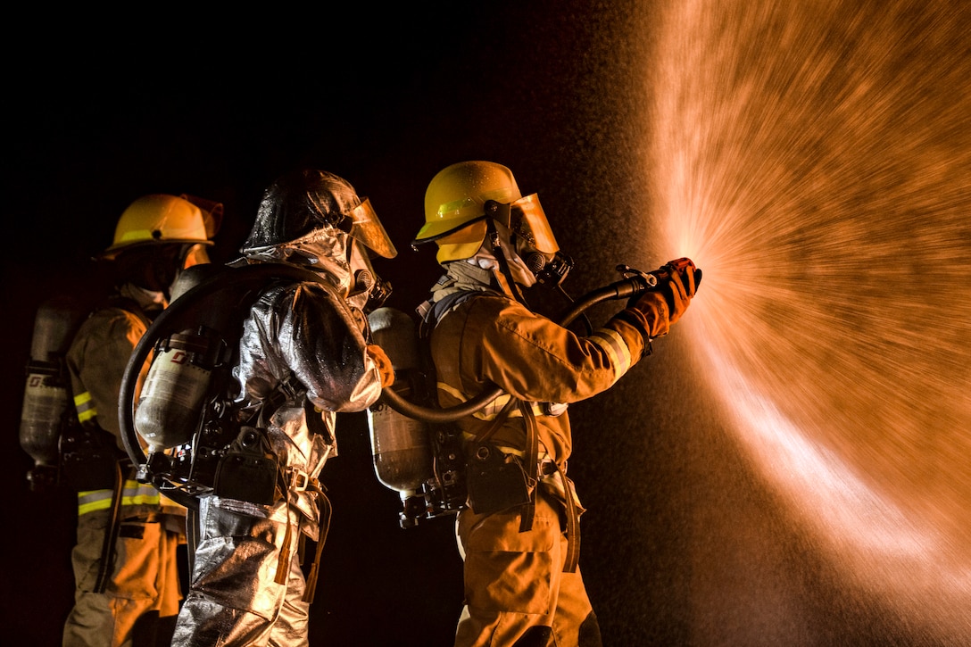 Three Marines spray water from a hose.