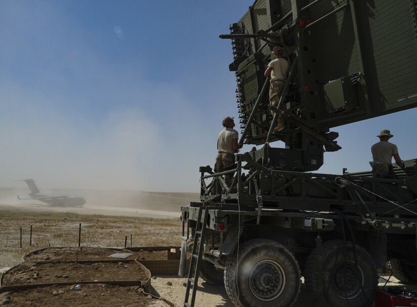 A U.S. Air Force C-17 Globemaster departs while U.S. Airmen from the 727th Expeditionary Air Control Squadron erect an antenna at a coalition airfield in Northeast Syria