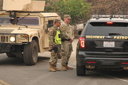 California Army National Guardsmen Sgt. Jesus Valencia and Spc. Cameron Hodges of the 270th Military Police Company, 185th Military Police Battalion, 49th Military Police Brigade, update  a Shasta County sheriff July 31 at the Keswick Dam in Redding, California, one of nearly three dozen traffic control points manned by the military police on their first days of activation for the Carr Fire.