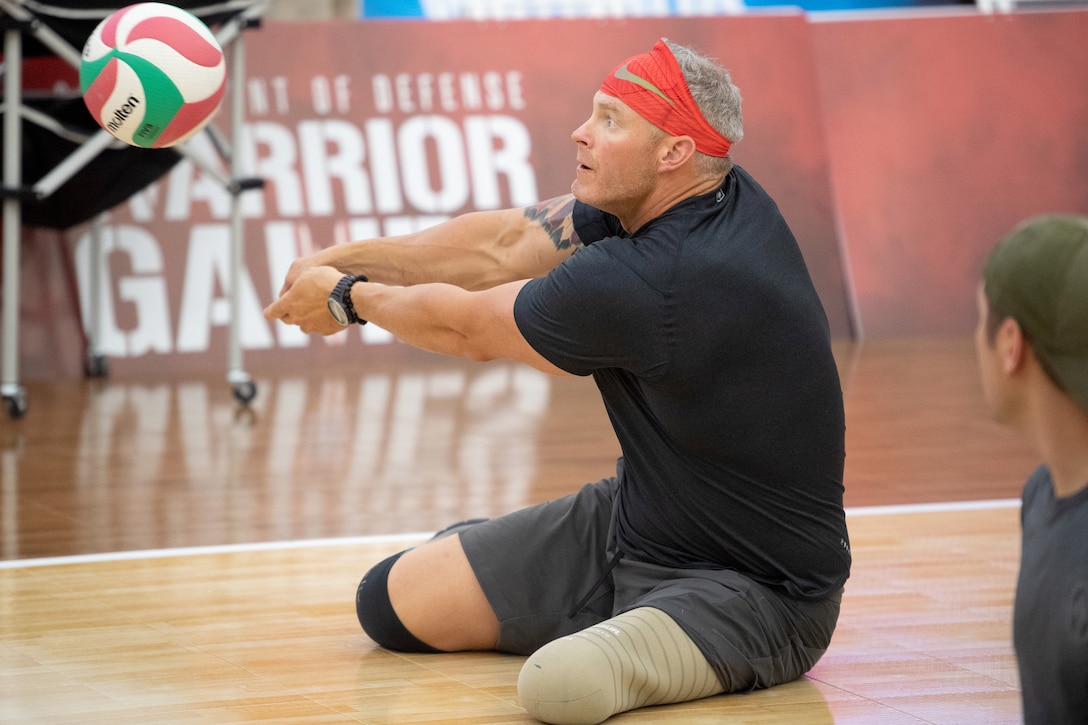 A man sits and hits a volleyball.