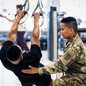 Asian male Physical Therapist wearing OCP training with a male ROTC Cadet wearing APFU inside during the daytime.